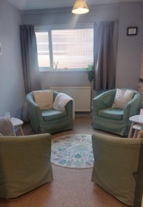 This room has 4 armchairs a small round rug and some stacked side tables to the side. There is a large window letting in plenty of natural light. 