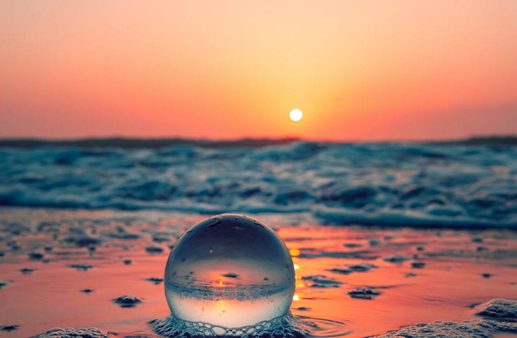 Image of a glass orb on a beach with the sea under a setting sun. The image gives a sense of serenity and relaxation.