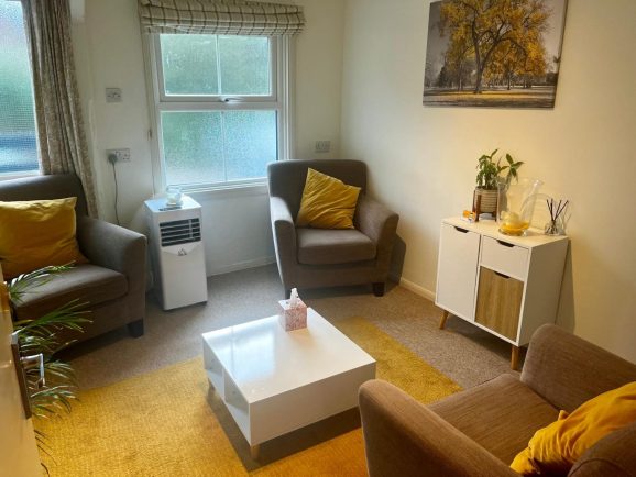 a room with two chairs face one chair. There is a while square coffee table in the centre of the room. There are orange accessories decorating the room.